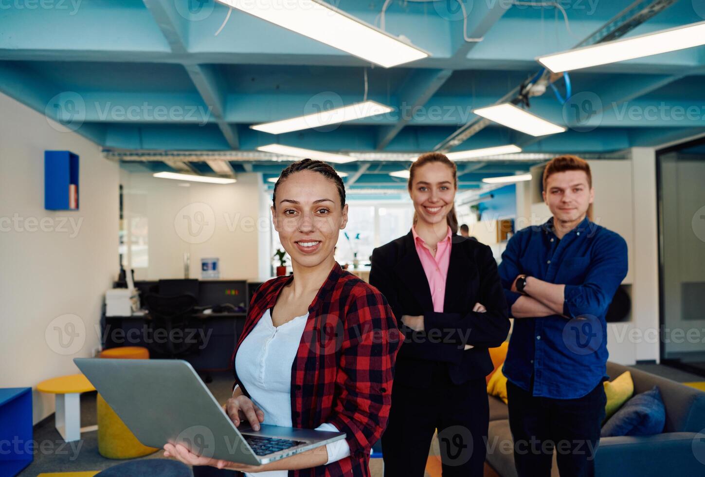 A young team of business professionals poses for a startup office portrait, exuding confidence and ambition, with one woman holding a laptop, symbolizing innovation and collaboration in photo