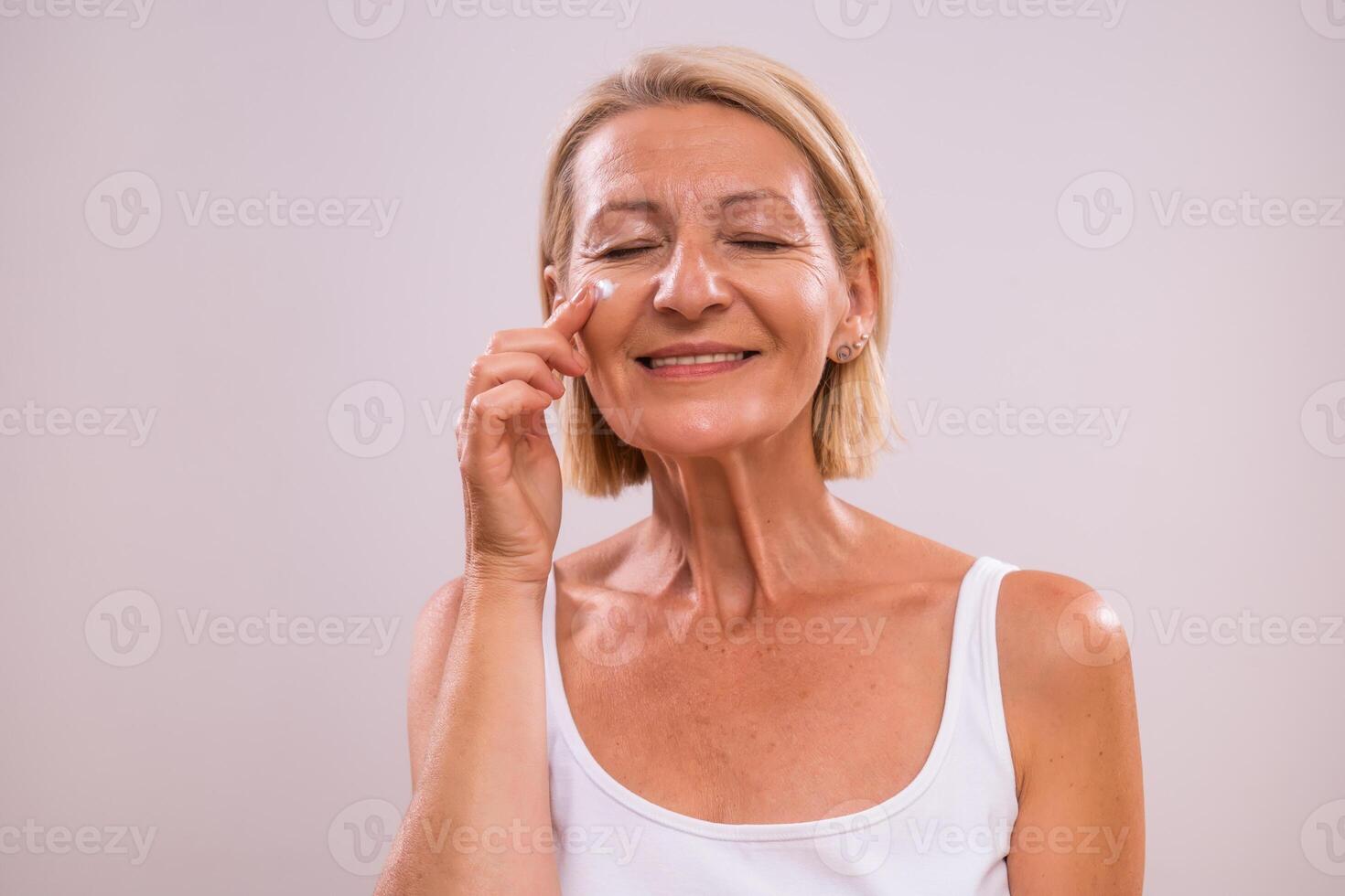 Portrait of beautiful mature woman applying moisturizer on her face. photo