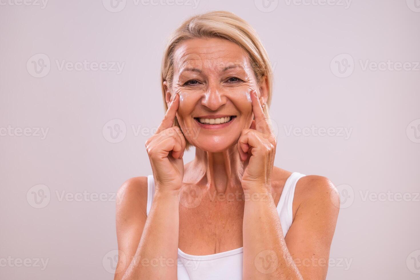 Portrait of beautiful mature woman applying moisturizer on her face. photo