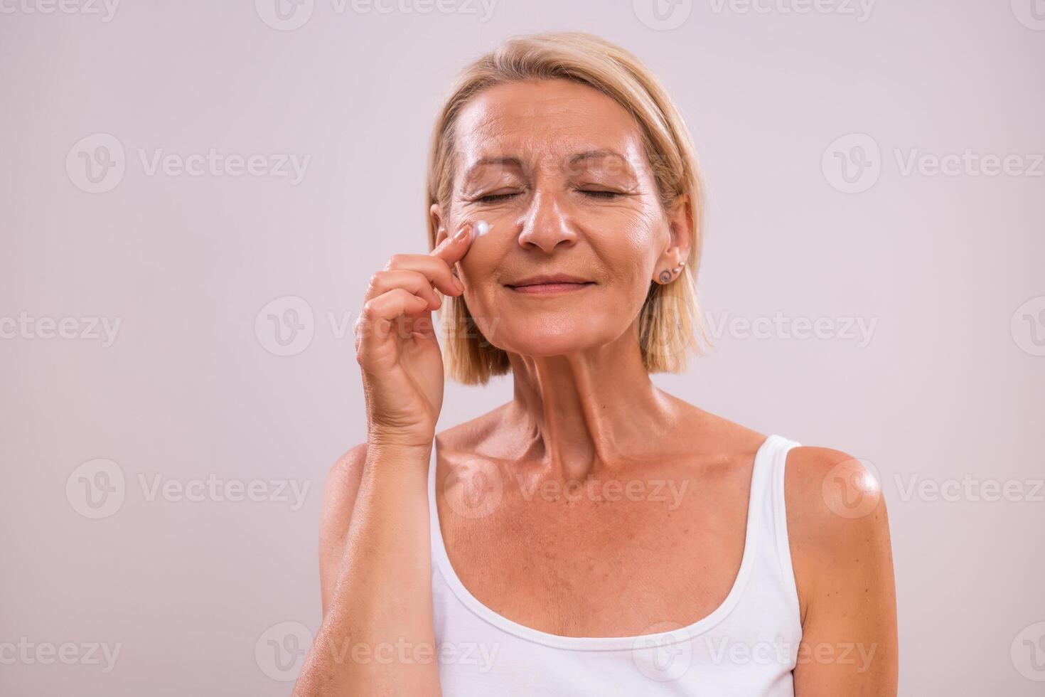 Portrait of beautiful mature woman applying moisturizer on her face. photo