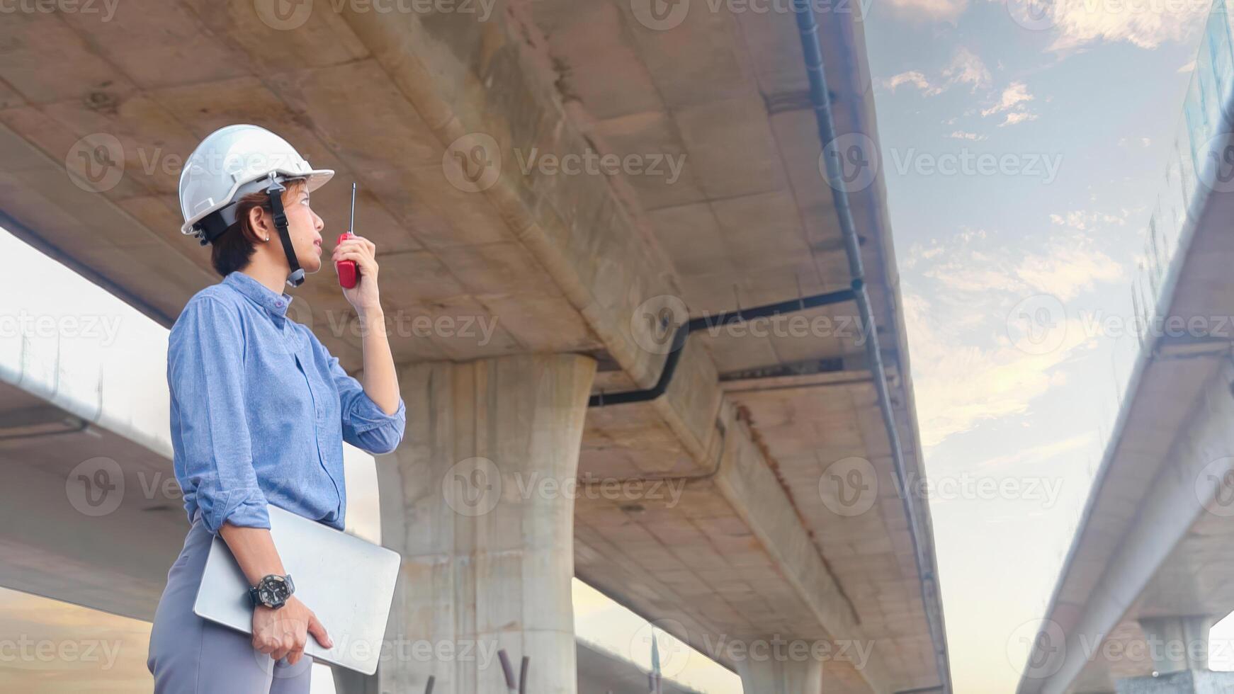 Asian female engineer using walkie talkie at construction site Standing near the concrete road, highway bridge. photo
