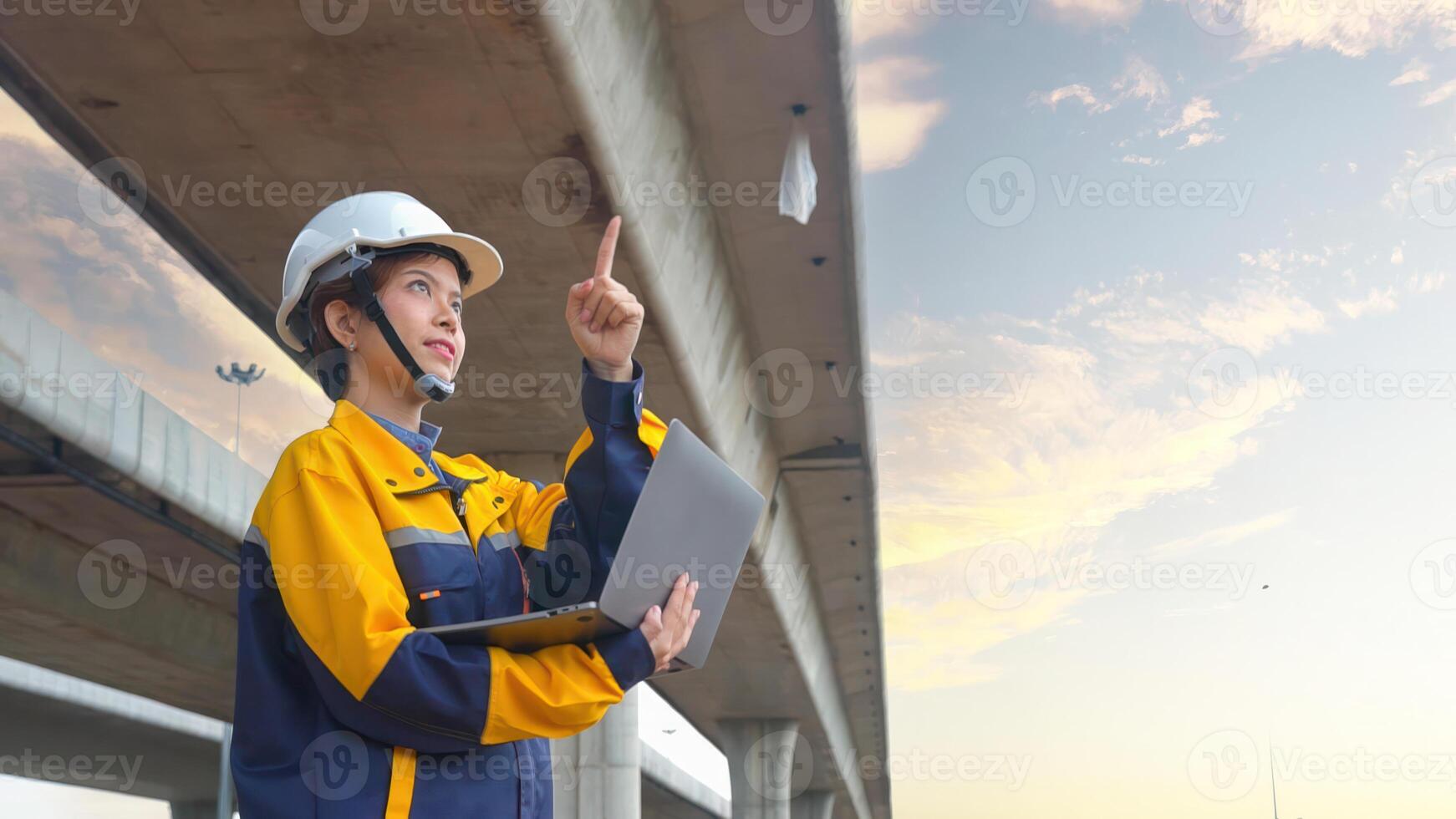 Asian female civil engineer using laptop computer standing on road construction site to supervise the construction of a new road. photo