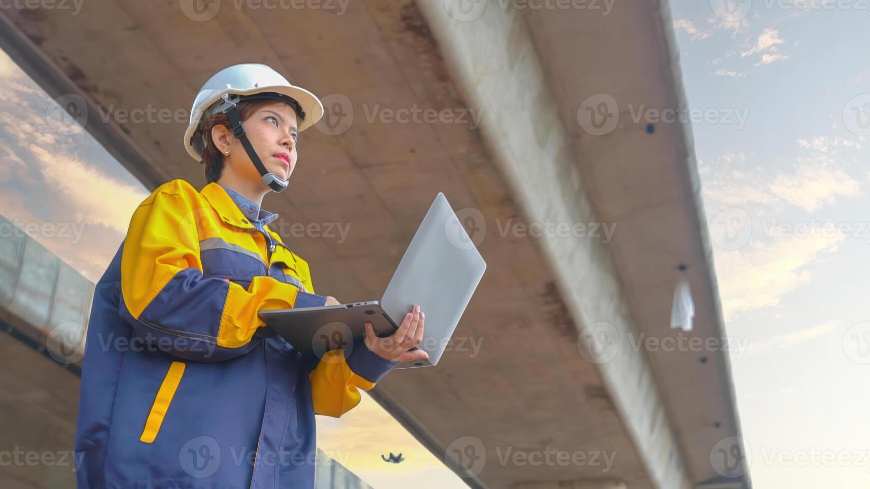 Asian female engineer Wear a yellow safety suit. Use a laptop to inspect highway construction work. photo