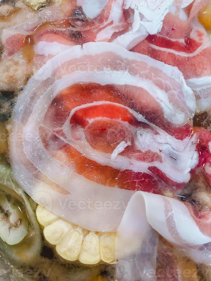 Uncooked bacon slices in hot soup. photo