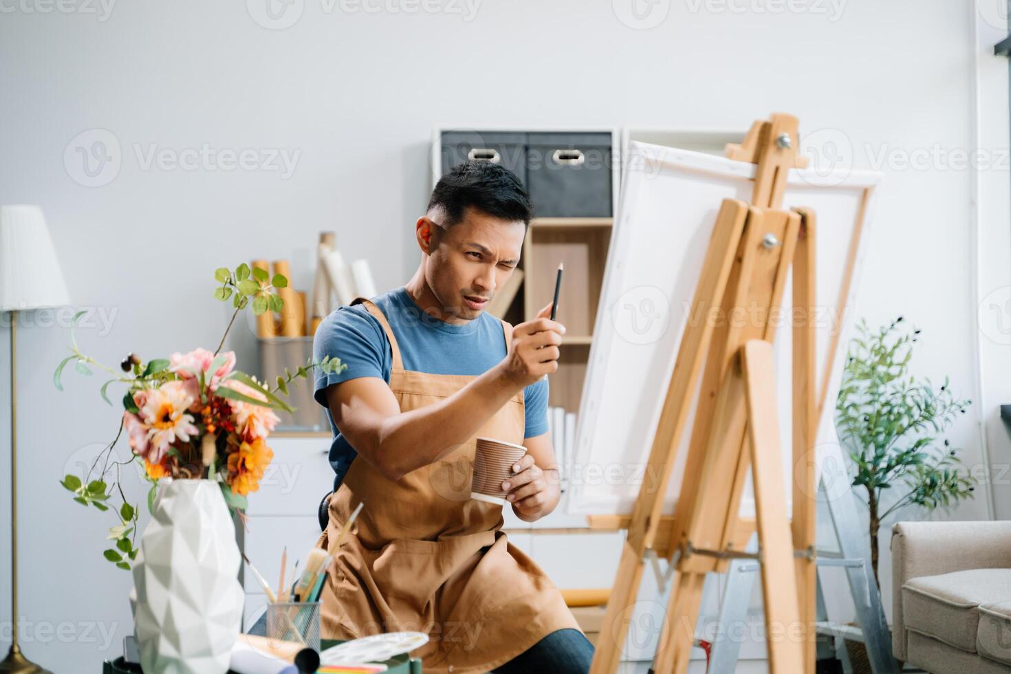 Asian male painter do artwork in art workshop, painting supplies, oil pastels, two canvas easel, creative space with paintbrush in art studio photo