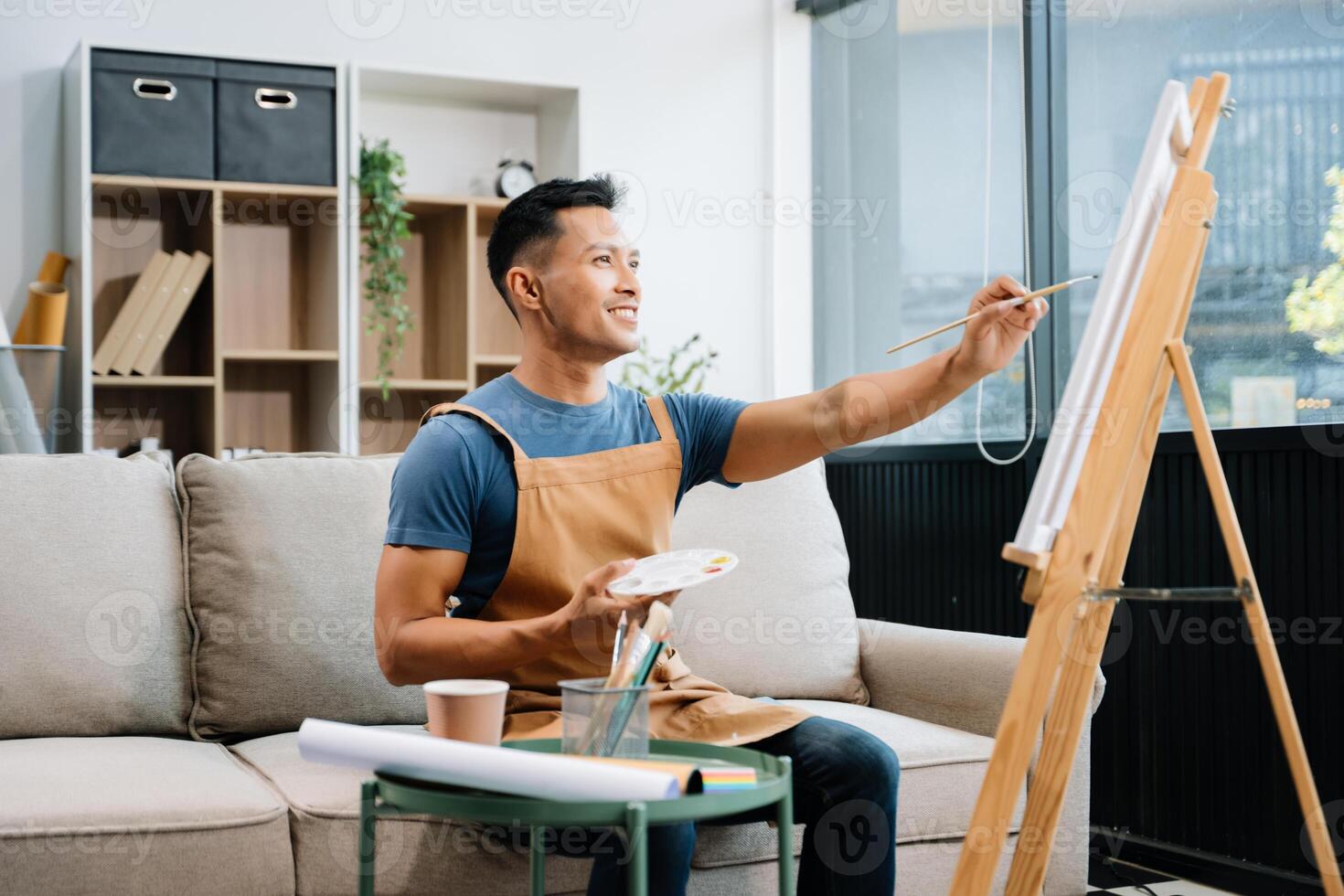 Asian male painter do artwork in art workshop, painting supplies, oil pastels, two canvas easel, creative space with paintbrush in art studio photo