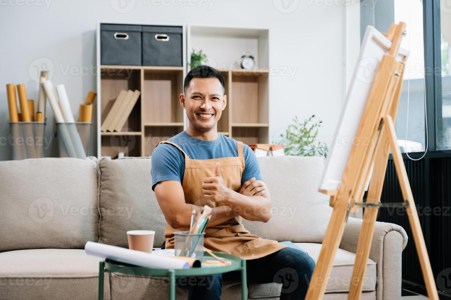 Asian male painter do artwork in art workshop, painting supplies, oil pastels, two canvas easel, creative space with paintbrush in art studio photo
