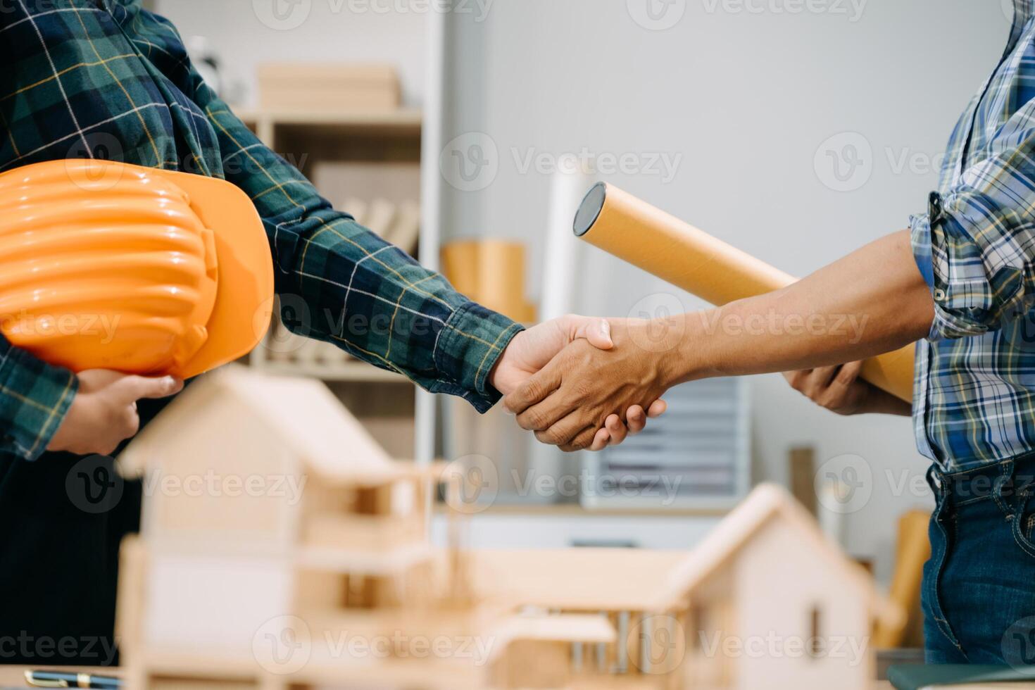 Construction team shake hands greeting start new project plan behind yellow helmet on desk in office center to consults about their building project. photo