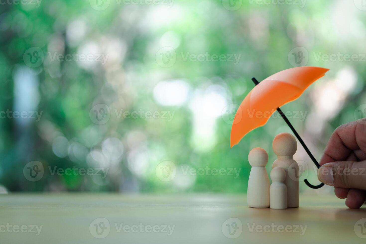 Wooden family figures under orange umbrella on a nature background. photo