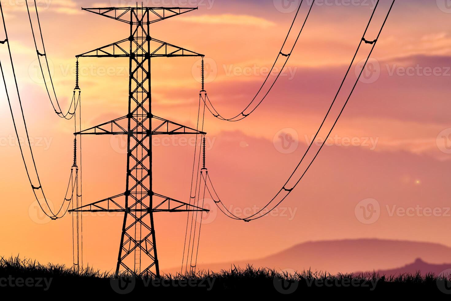 Silhouette of High Voltage Power Lines and Transmission Tower at Sunset with Vibrant Sky and Mountains in the Background photo