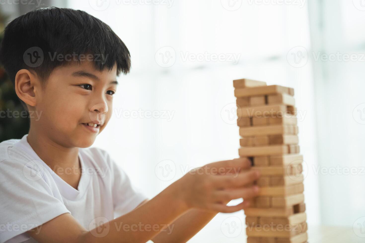 A young boy is playing with a wooden block tower. He is focused on the tower and he is enjoying himself photo