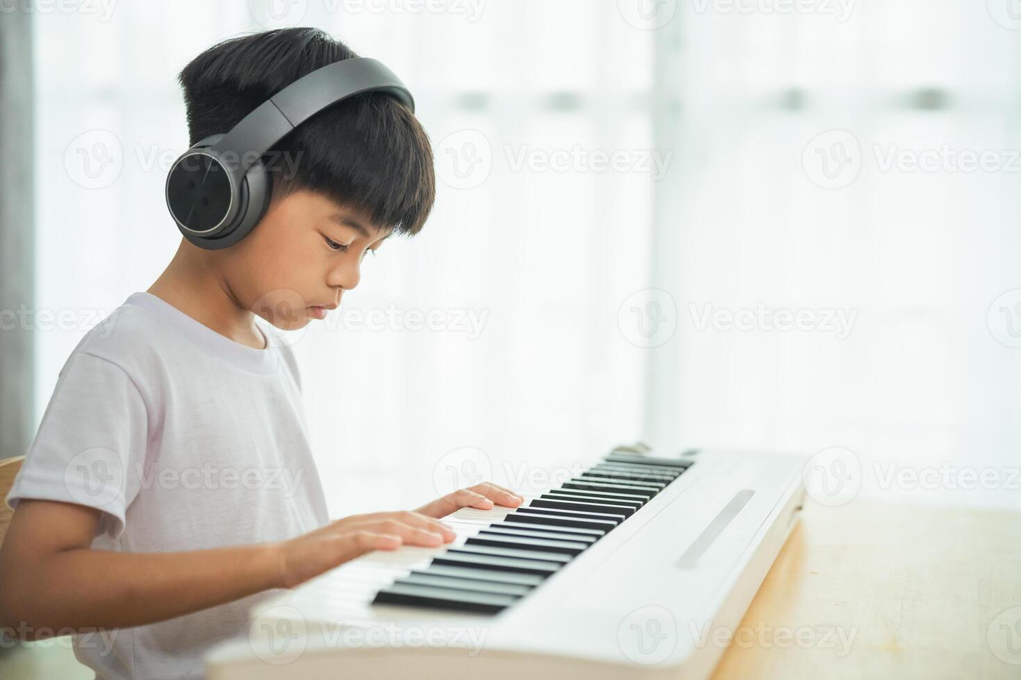 A young boy is playing the keyboard with headphones on. He is focused on the music and he is enjoying himself photo