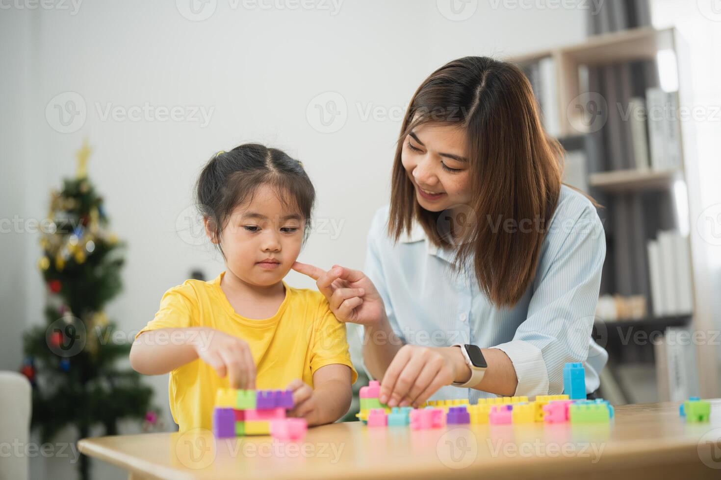 Asian woman and a child are playing with blocks. The woman is helping the child build a tower photo