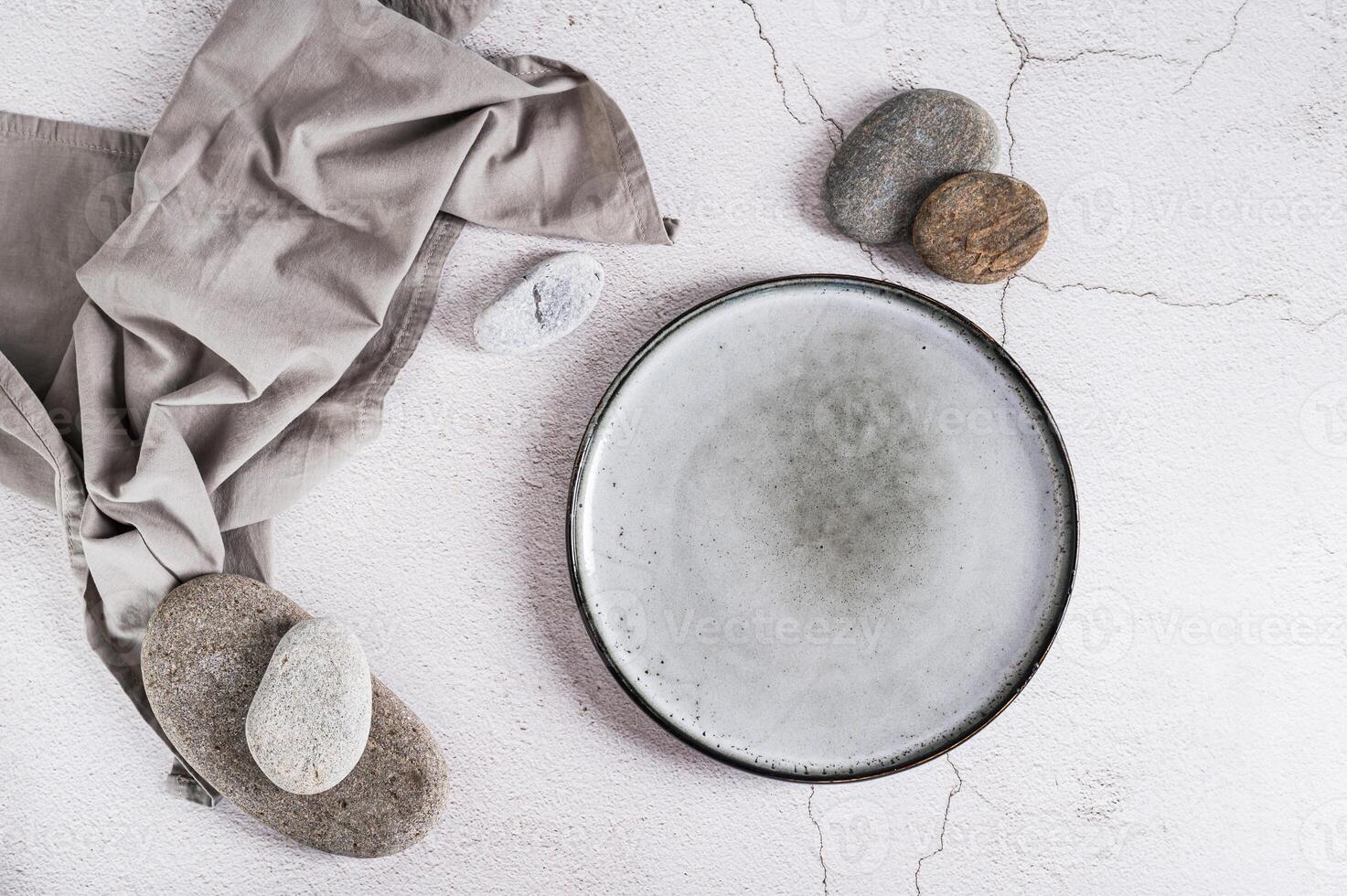Empty ceramic plate, stones and napkin on gray background top view photo