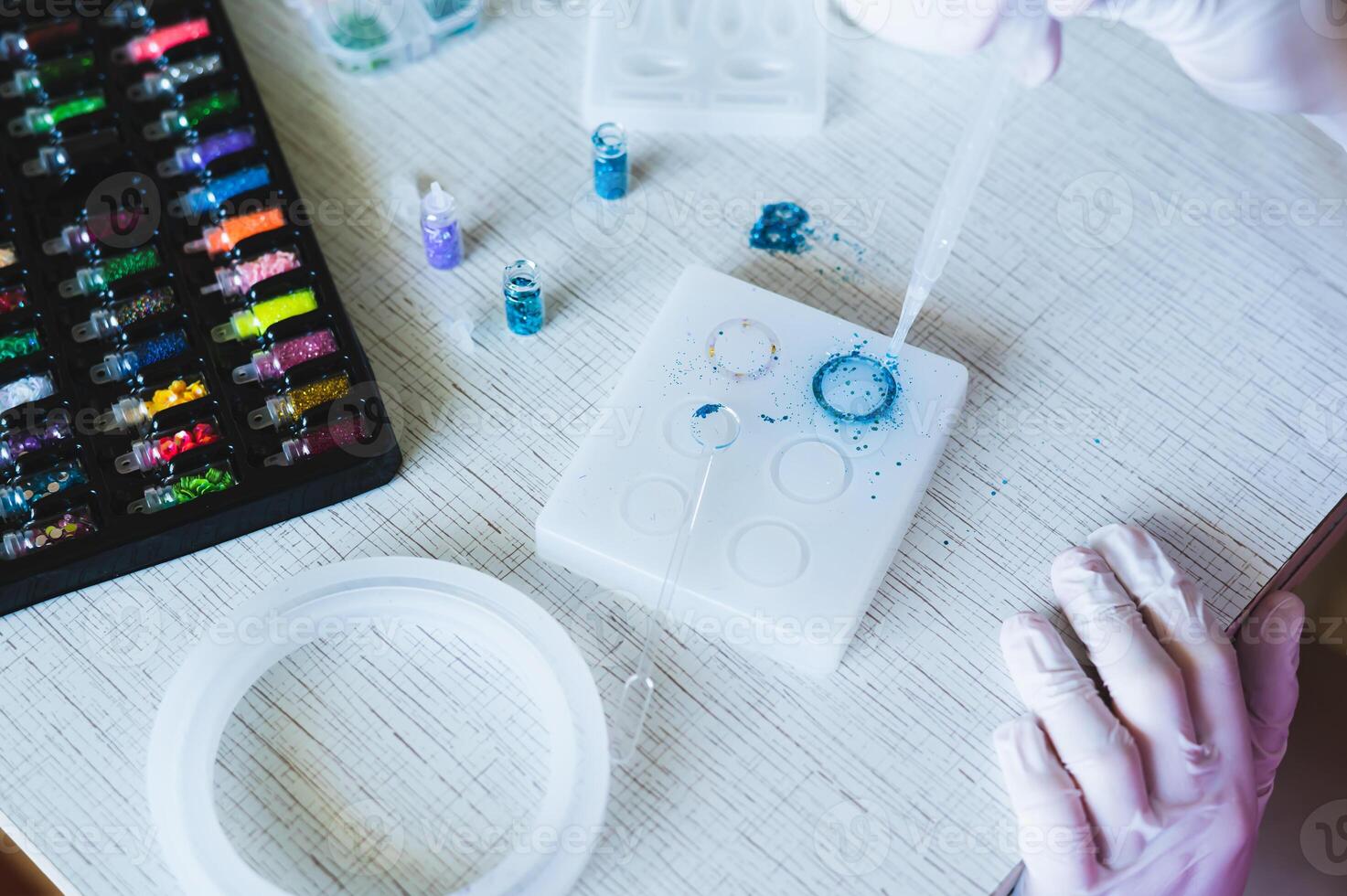 Children's hands in gloves fill a mold for making a ring with epoxy resin photo