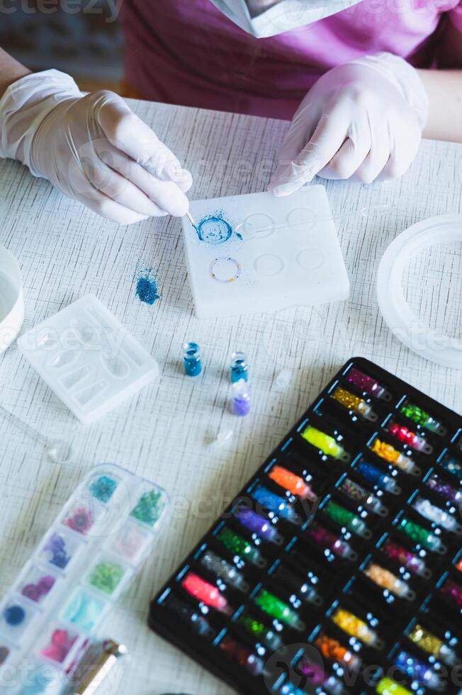 Children's hands in gloves fill an epoxy resin ring mold with decorative sparkles vertical view photo