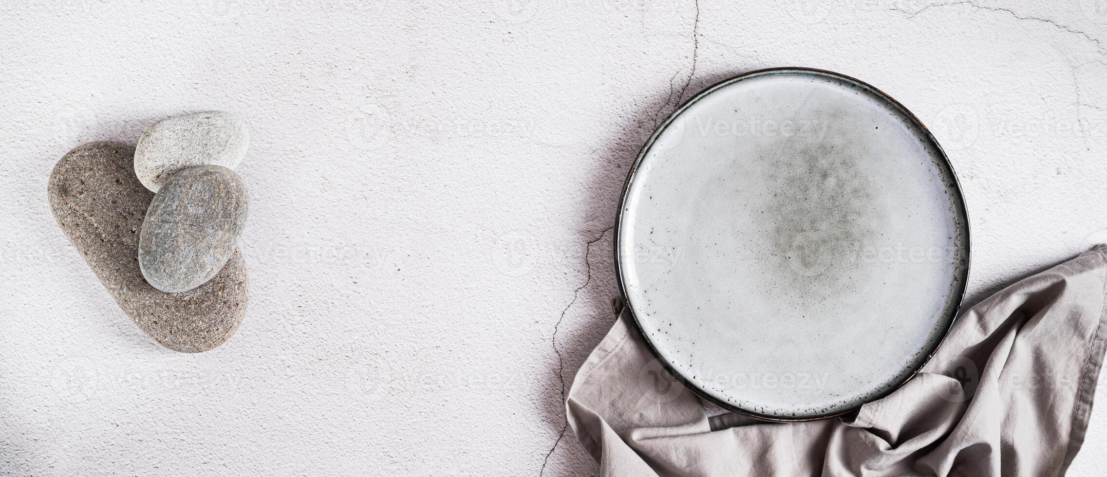 Empty ceramic plate, stones and napkin on gray background top view web banner photo