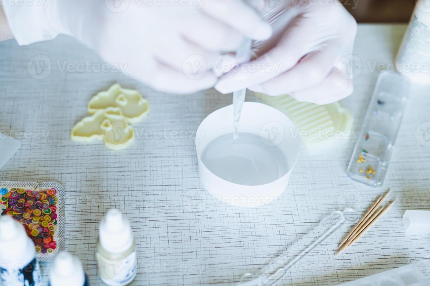 Female hands in gloves fill a bowl with epoxy resin for making earrings photo