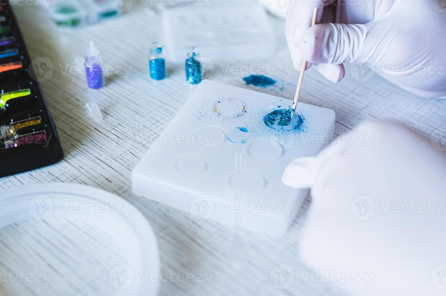 Children's hands in gloves fill an epoxy resin ring mold with decorative sparkles photo