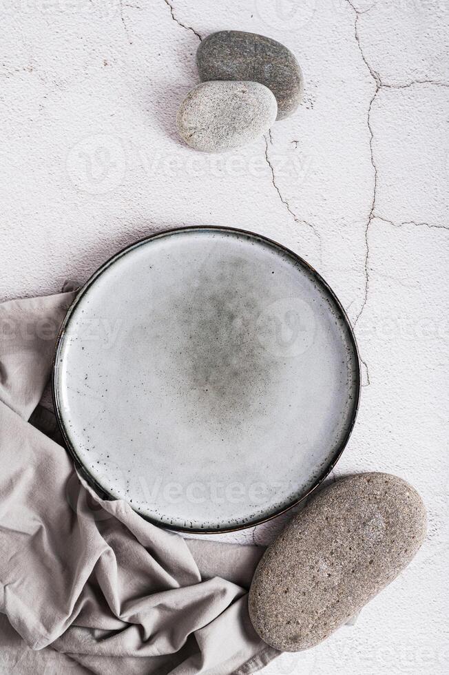 Empty ceramic plate, stones and napkin on gray background top and vertical view photo