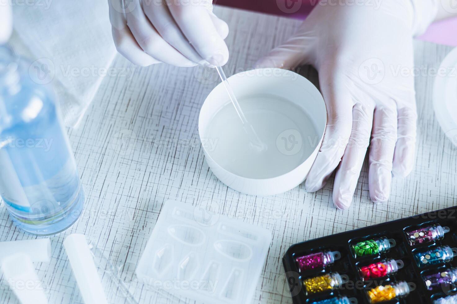 Female hands in gloves mix epoxy resin in a bowl for making jewelry photo