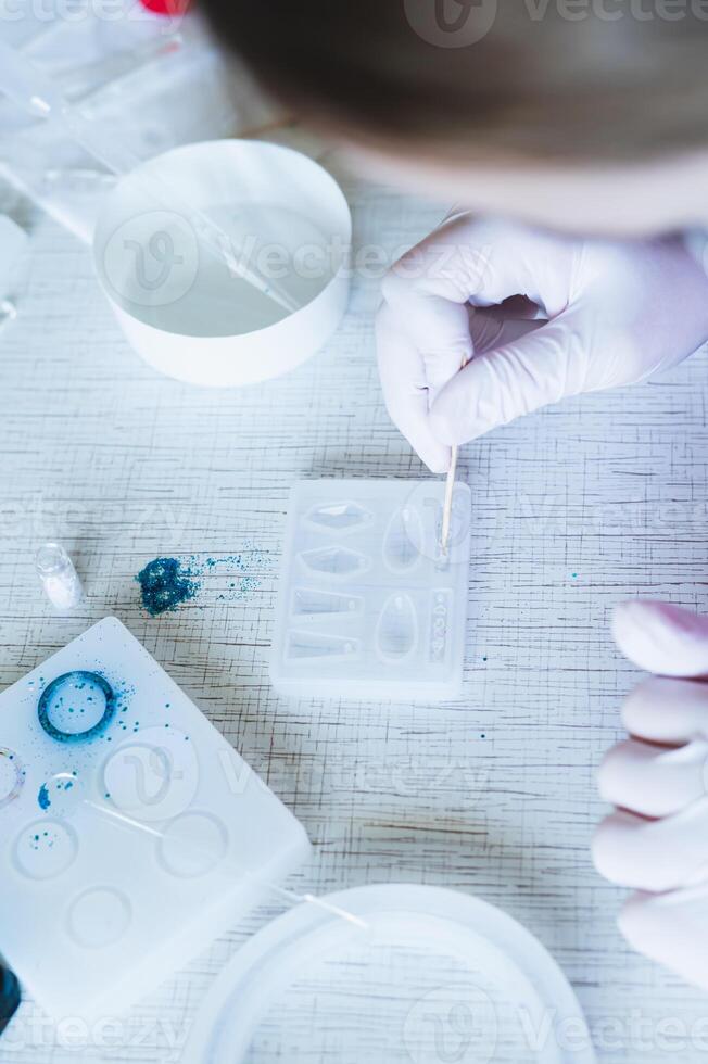 Female hands in gloves decorate earrings made of epoxy resin in the form vertical view photo