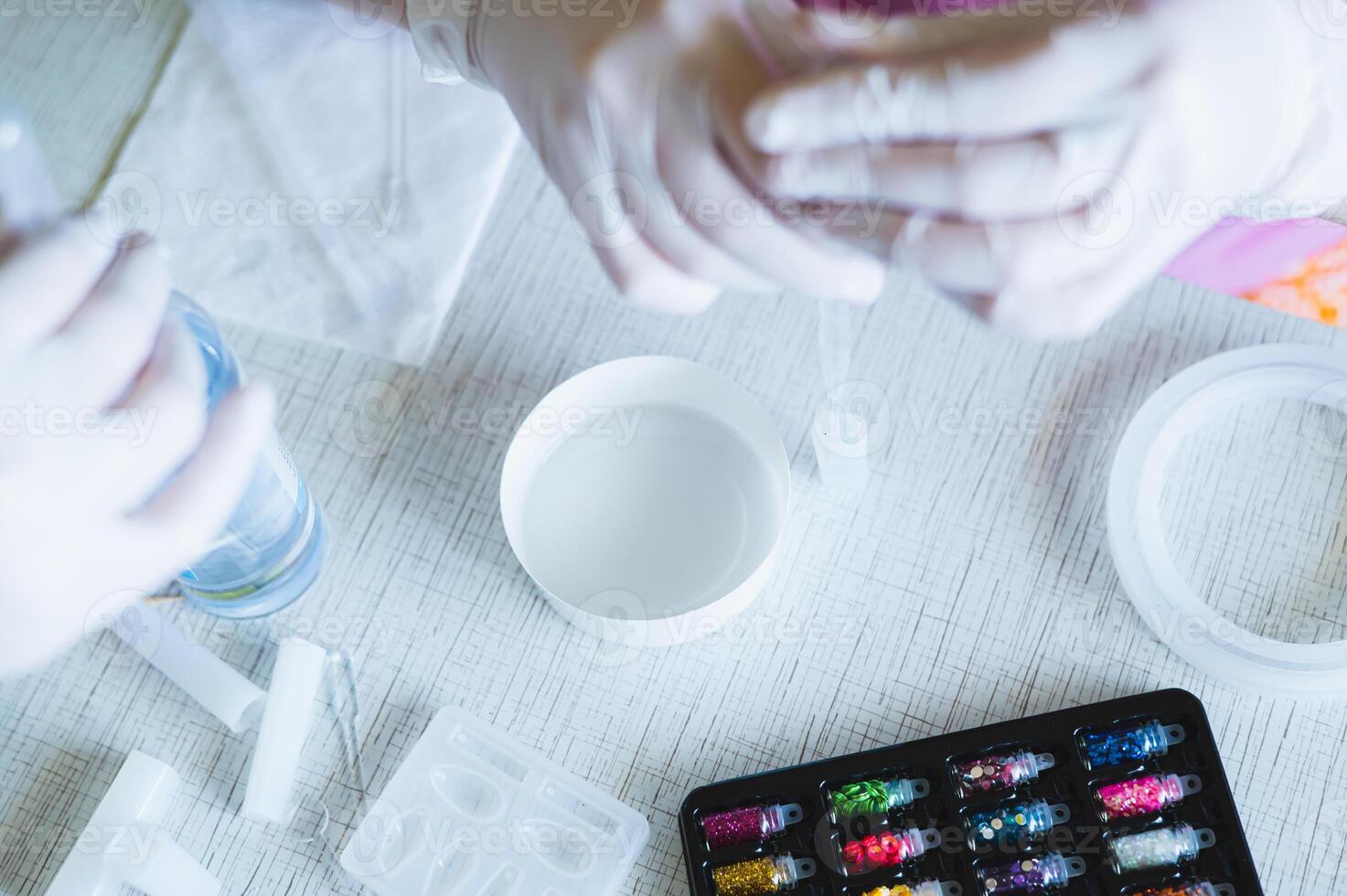 Female hands in gloves fill a pendant mold with epoxy resin photo
