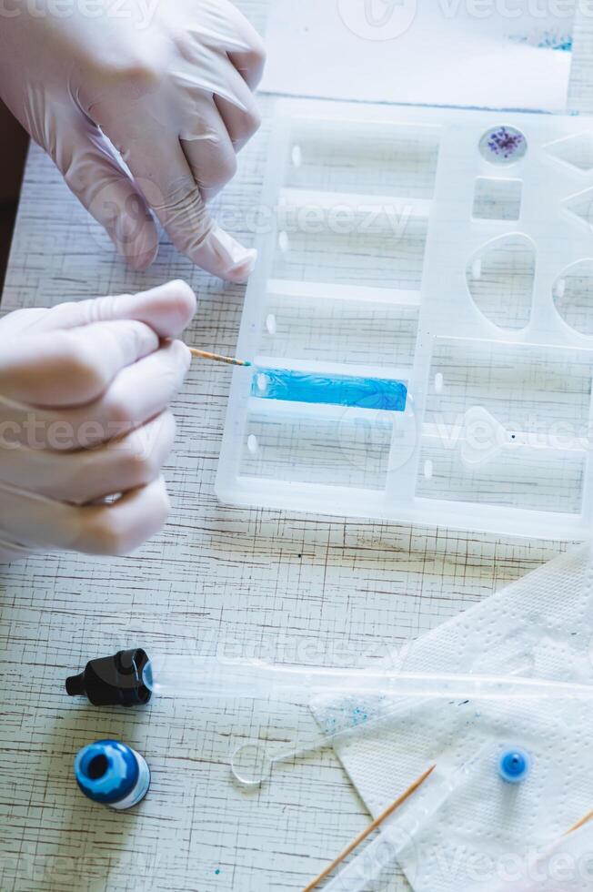 Children's hands in gloves fill a pendant mold with epoxy resin and paint vertical view photo