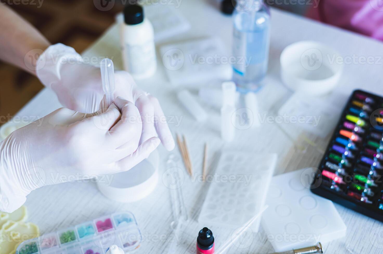 Female hands in gloves pour epoxy resin into a bowl for making jewelry photo