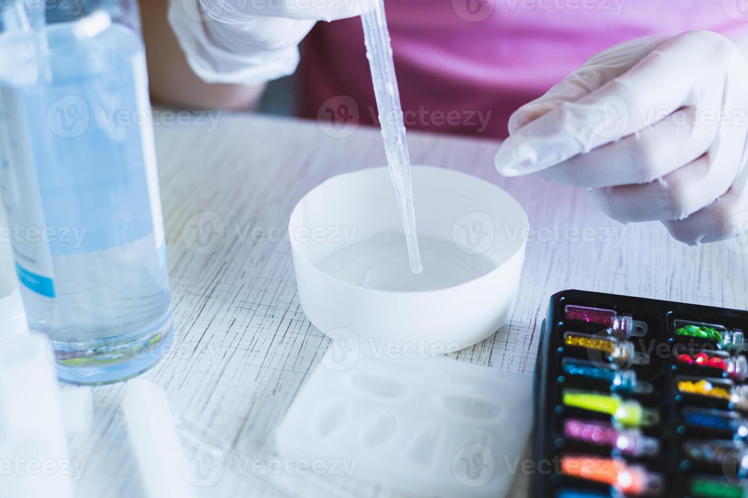 Female hands in gloves squeeze epoxy resin from a pipette into a bowl for making jewelry photo