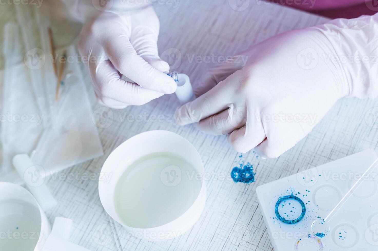 Female hands in gloves pour sparkles into a mold for making a pendant from epoxy resin photo