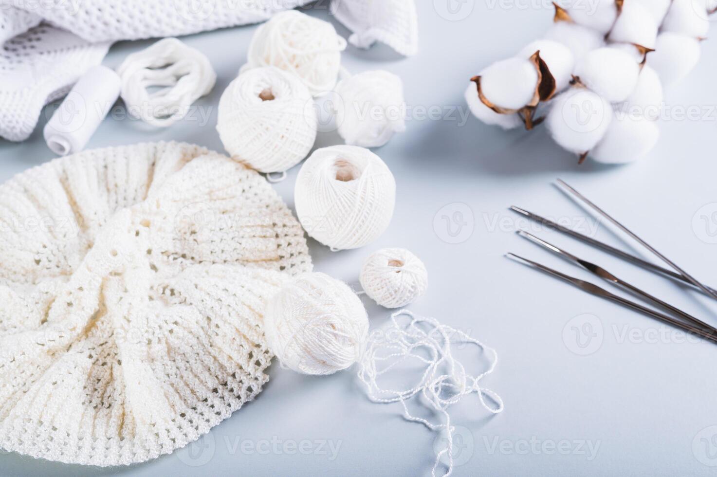 An uncrocheted beret, balls, hooks, needles and a cotton branch on a blue background photo