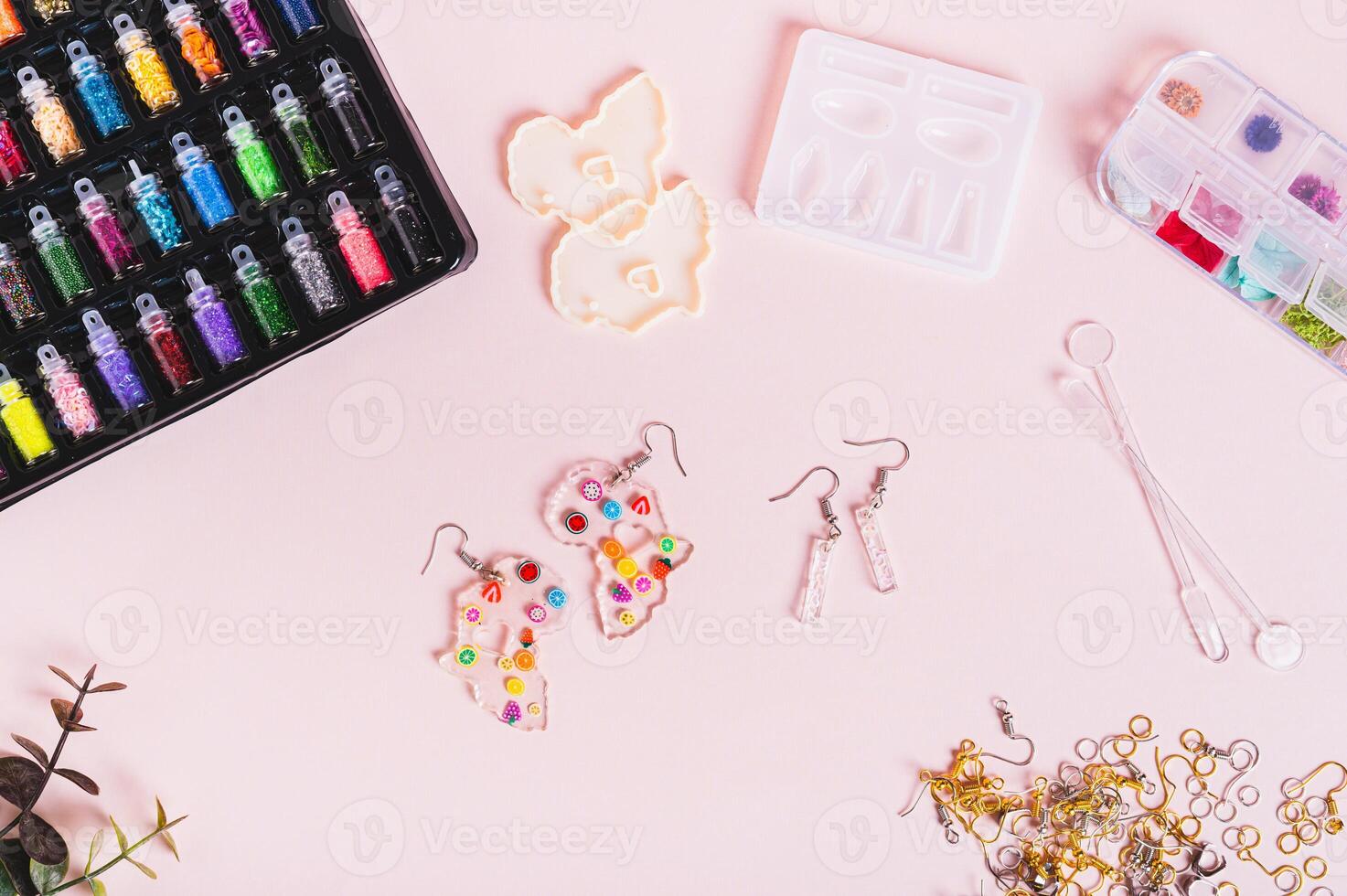 Earrings made of epoxy resin, molds and sparkles for making on a pink background top view photo