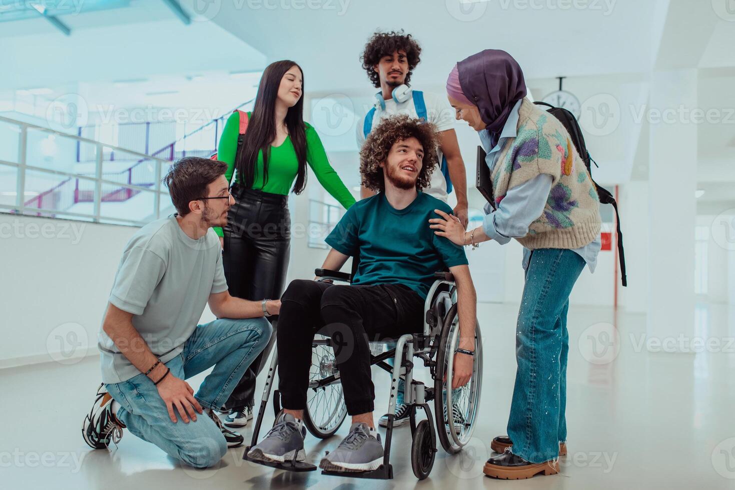 A diverse group of students including an African-American student and a Muslim wearing a hijab, support their friend with disability in a wheelchair in the hallway of a modern school. photo
