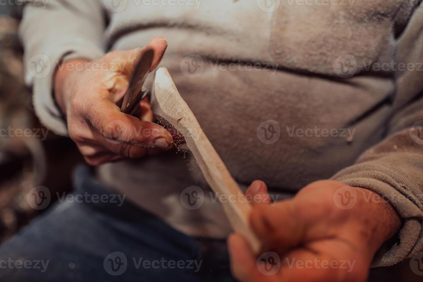 A senior man sitting in the workshop and processing wooden utensils in the old manual way photo