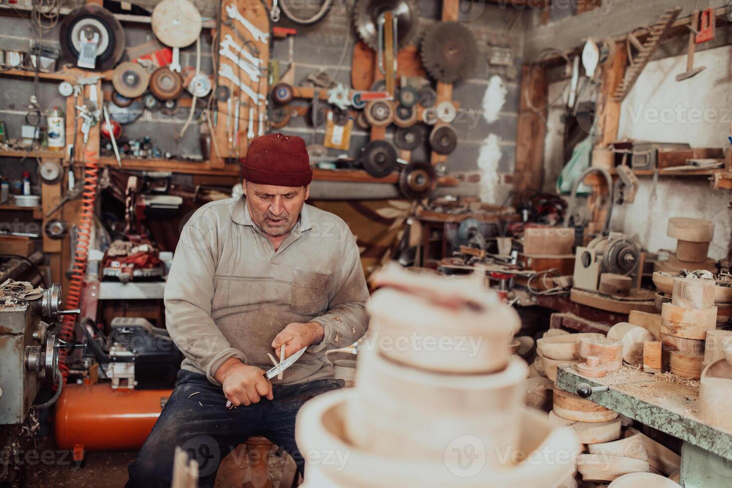 A senior man sitting in the workshop and processing wooden utensils in the old manual way photo