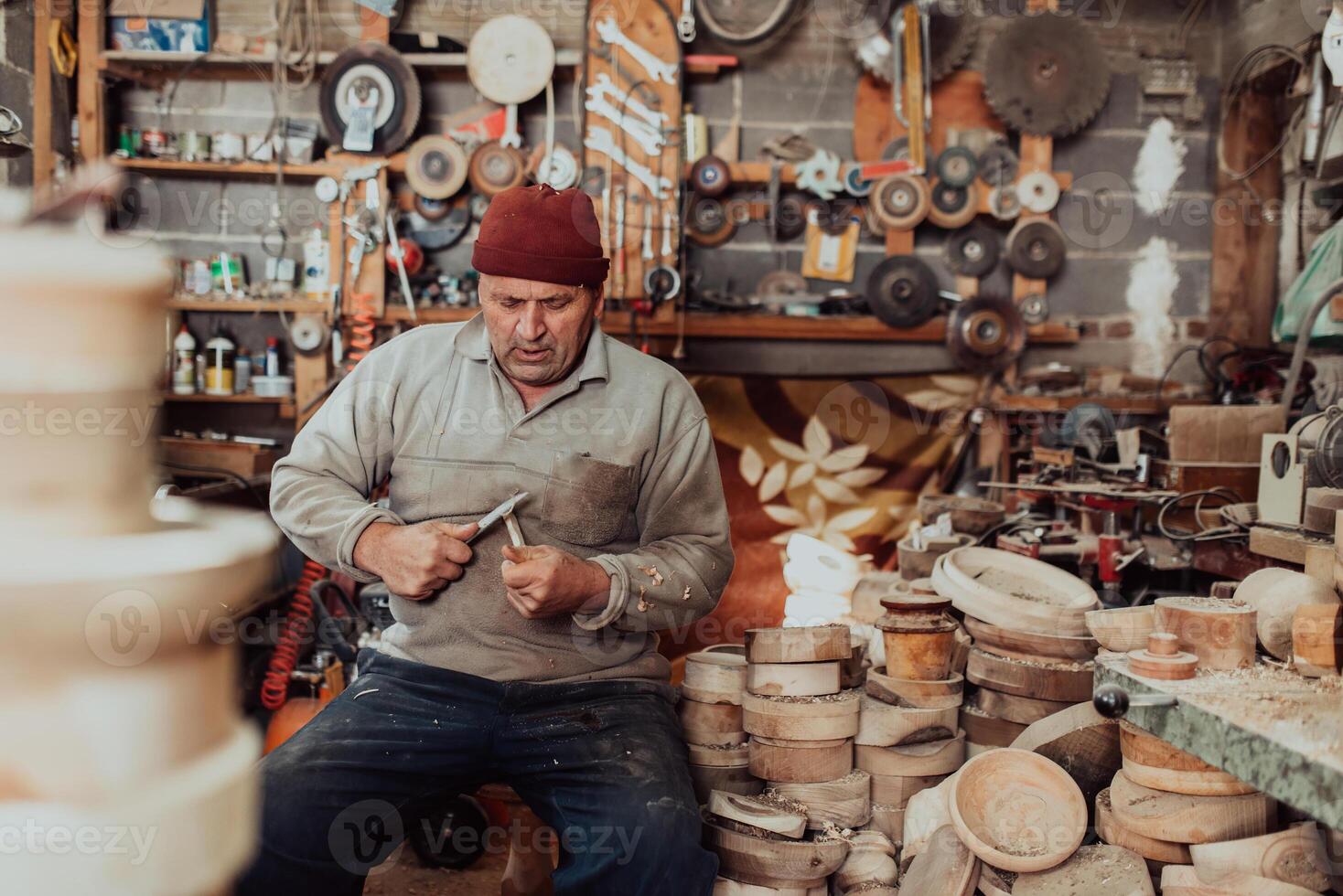 A senior man sitting in the workshop and processing wooden utensils in the old manual way photo