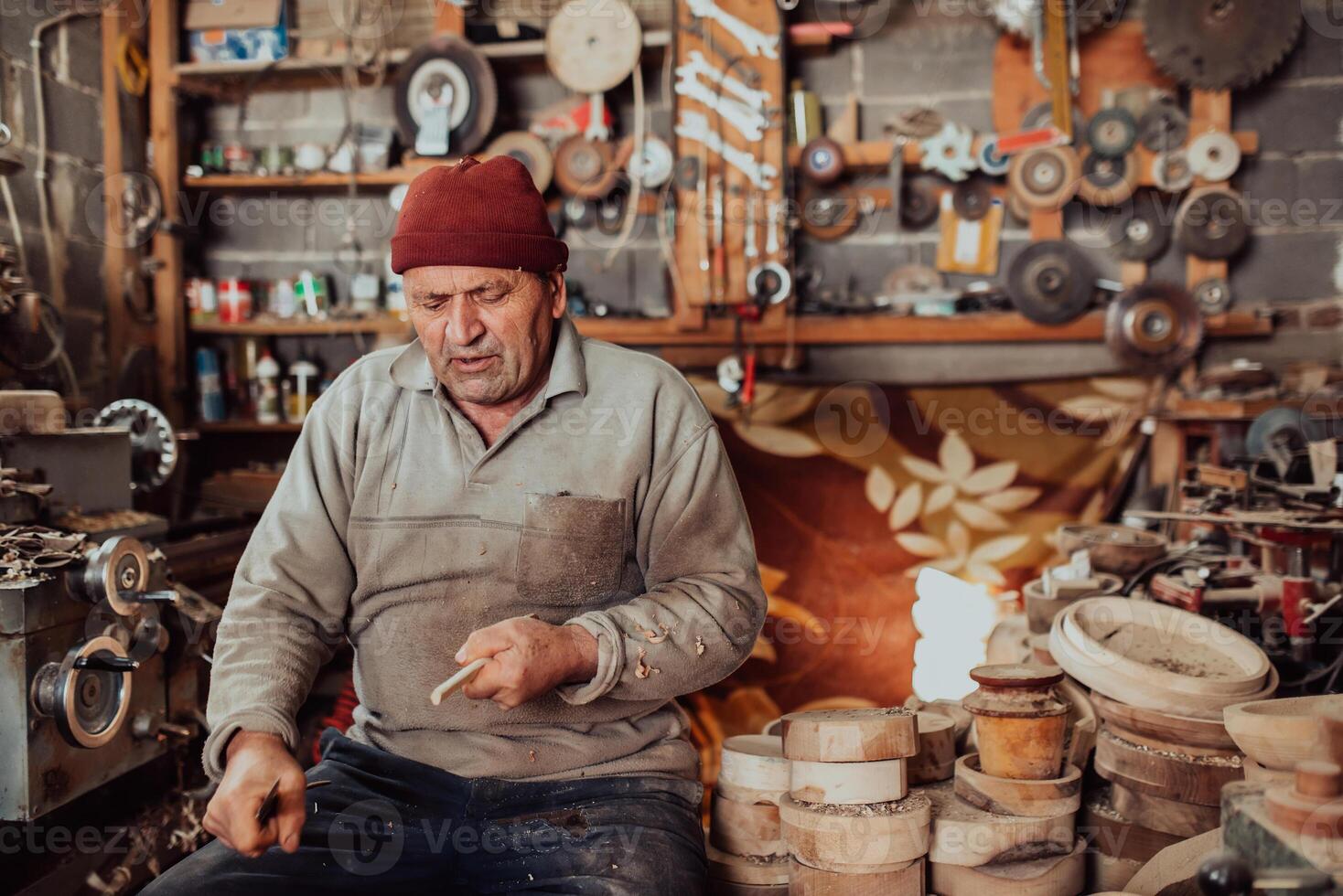 A senior man sitting in the workshop and processing wooden utensils in the old manual way photo