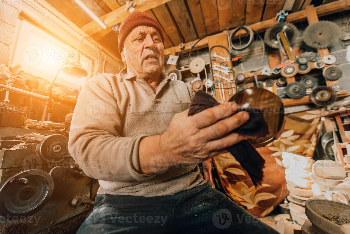 A senior man sitstingin the workshop and smearsing wooden utensils with linseed oil photo