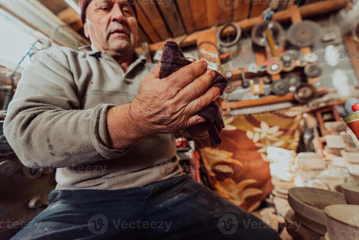 A senior man sitstingin the workshop and smearsing wooden utensils with linseed oil photo