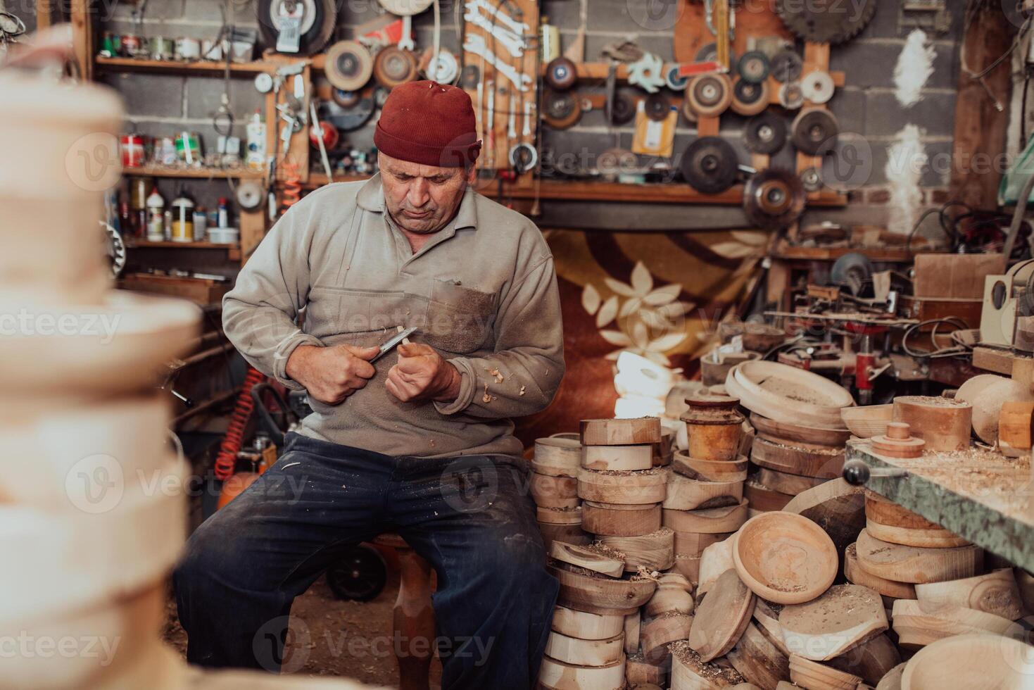 A senior man sitting in the workshop and processing wooden utensils in the old manual way photo