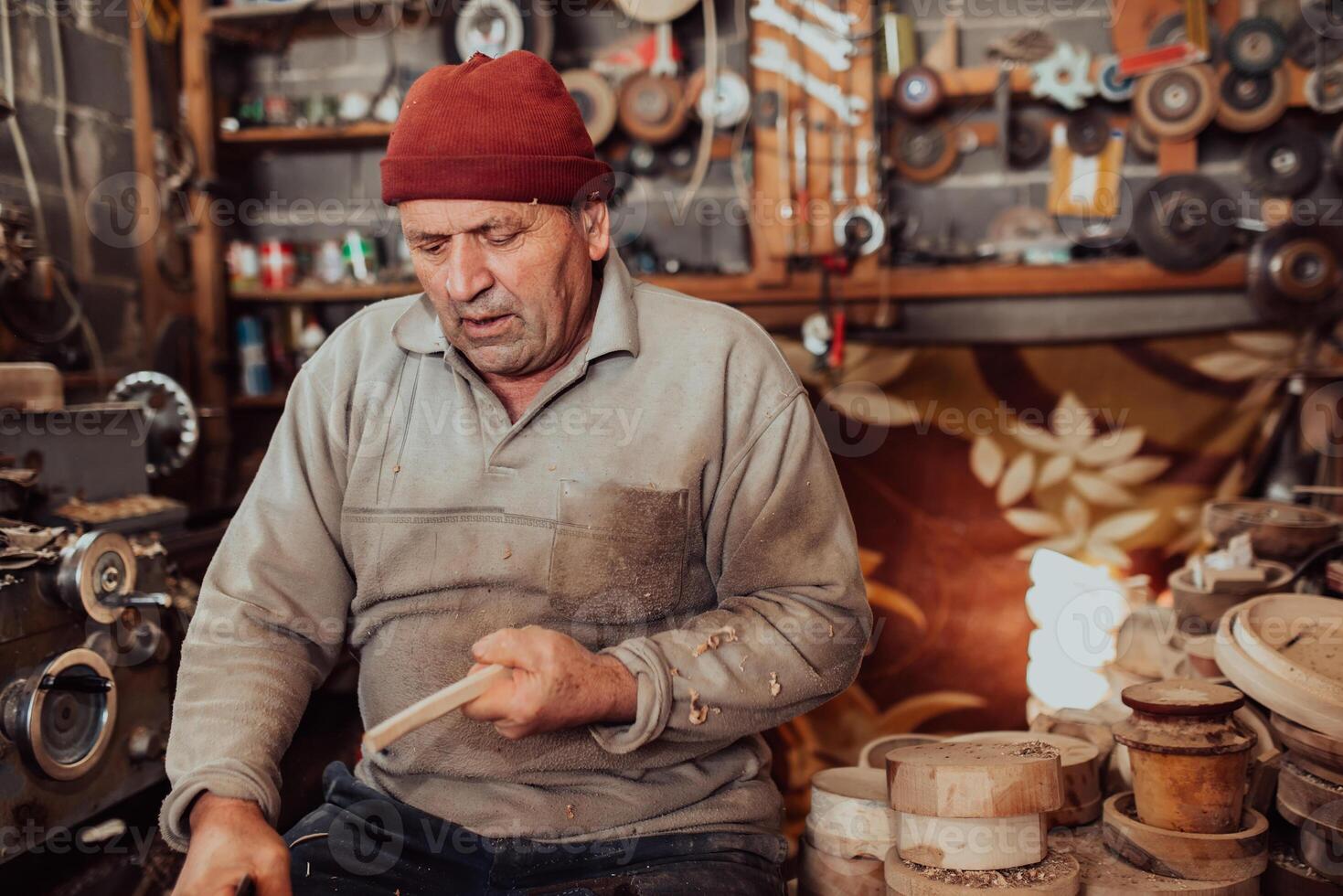A senior man sitting in the workshop and processing wooden utensils in the old manual way photo