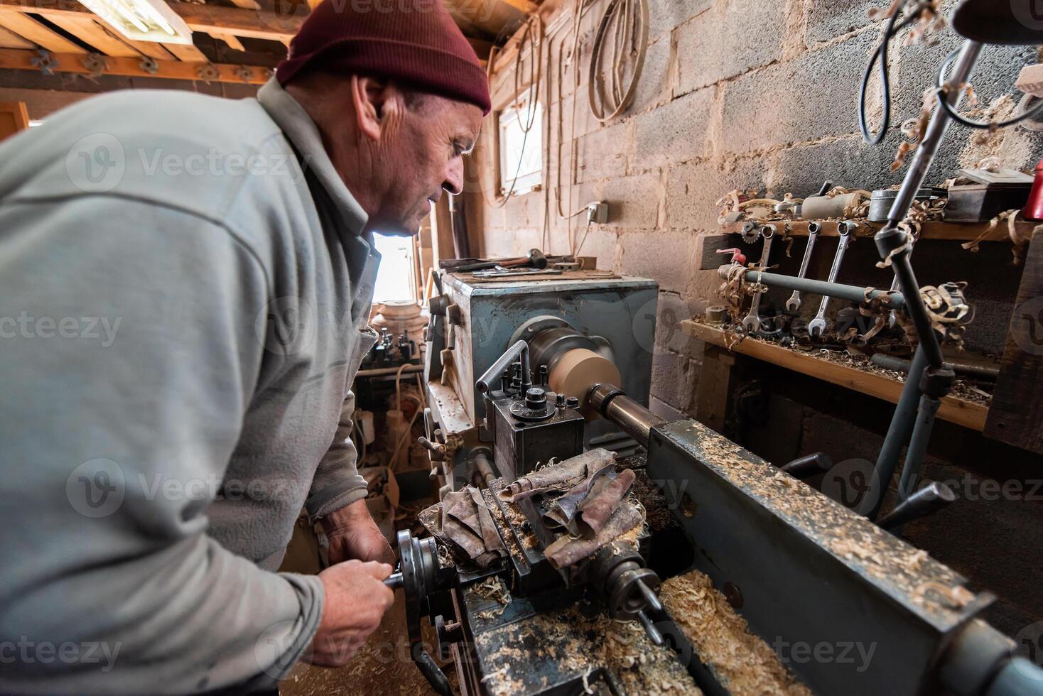 A senior man procesing wood on a lathe and making wooden dishes in the workshop photo