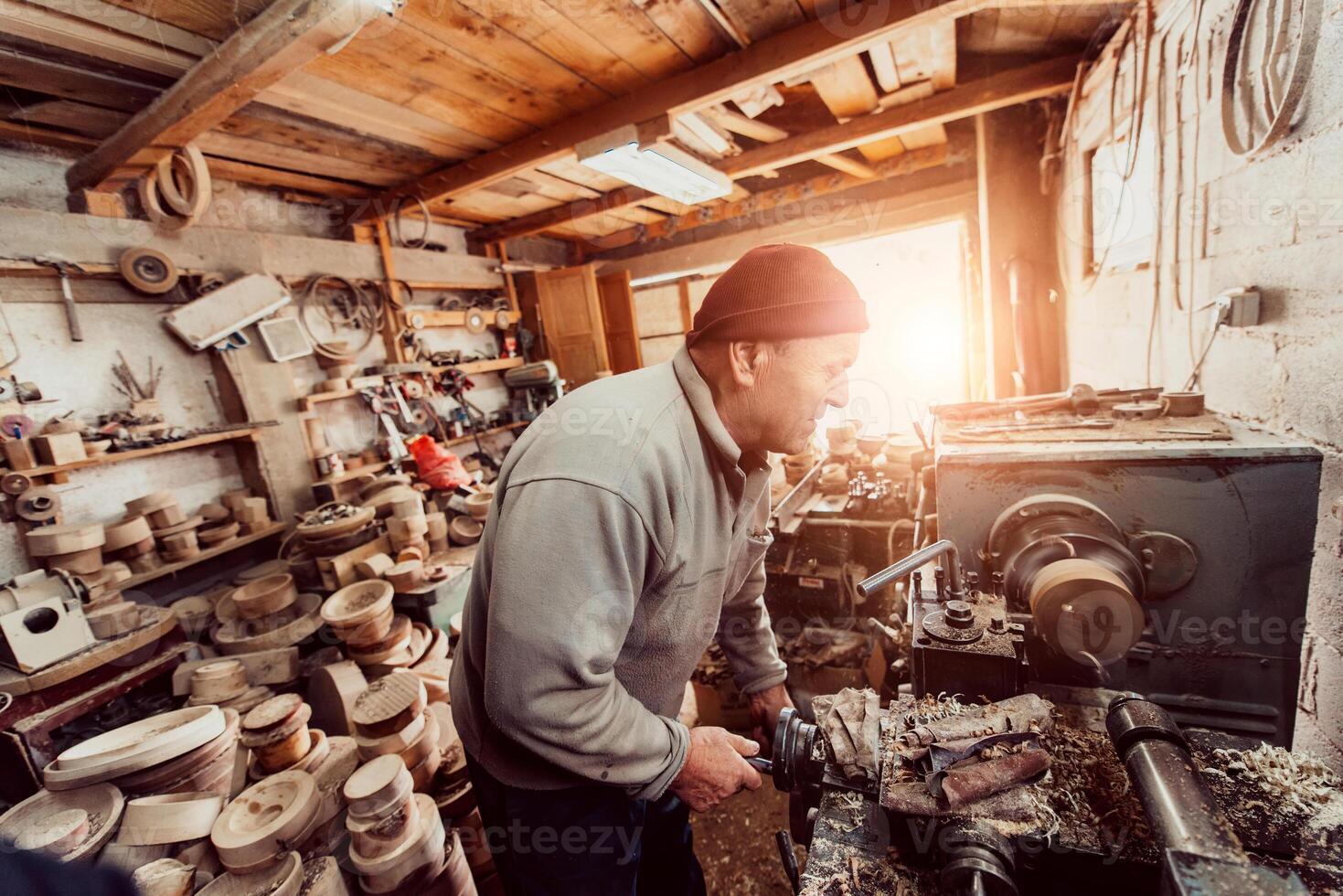 A senior man procesing wood on a lathe and making wooden dishes in the workshop photo