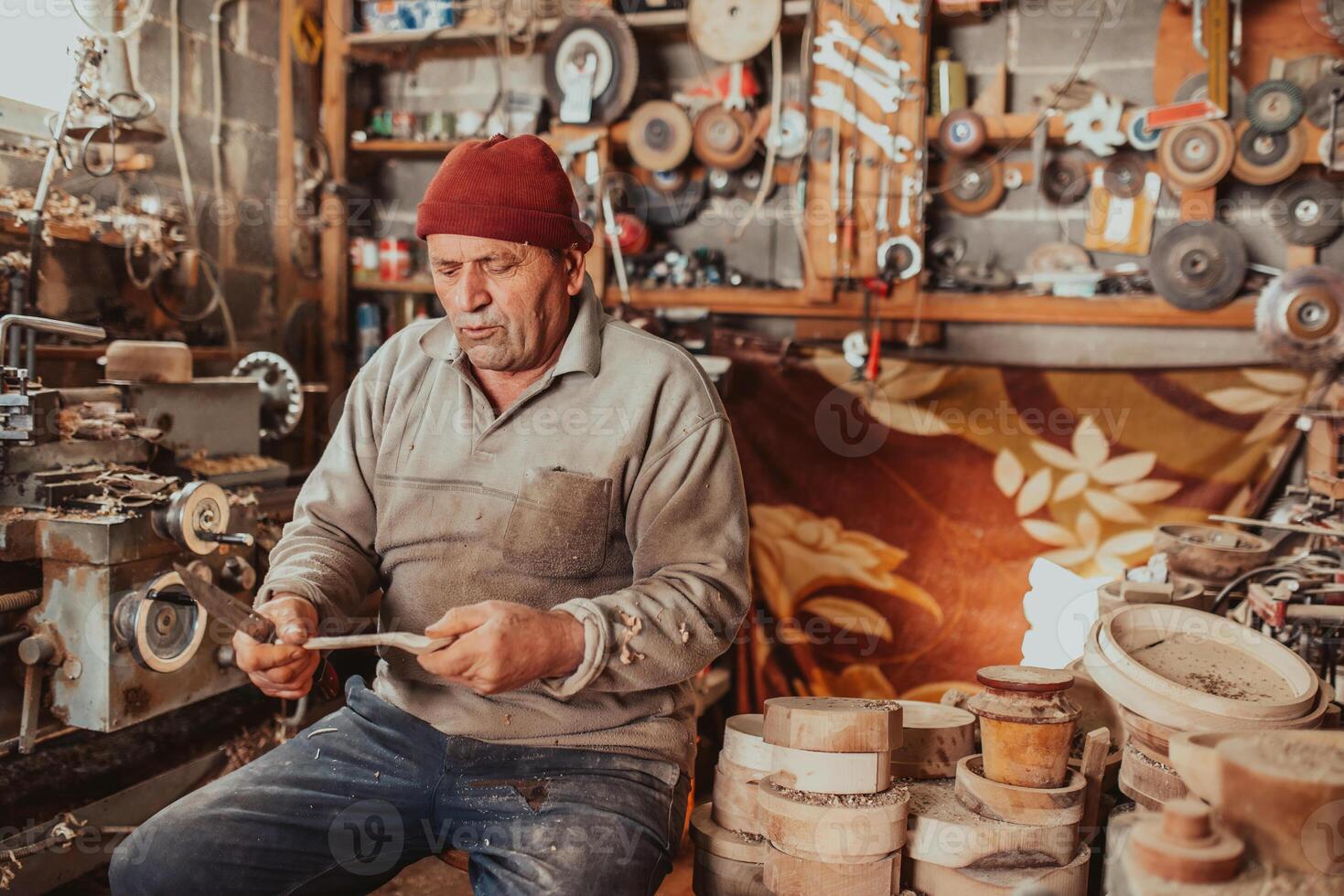 A senior man sitting in the workshop and processing wooden utensils in the old manual way photo