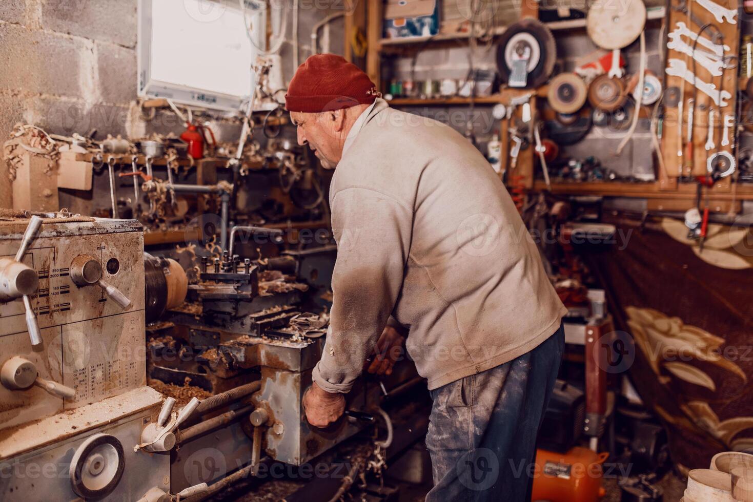 A senior man procesing wood on a lathe and making wooden dishes in the workshop photo