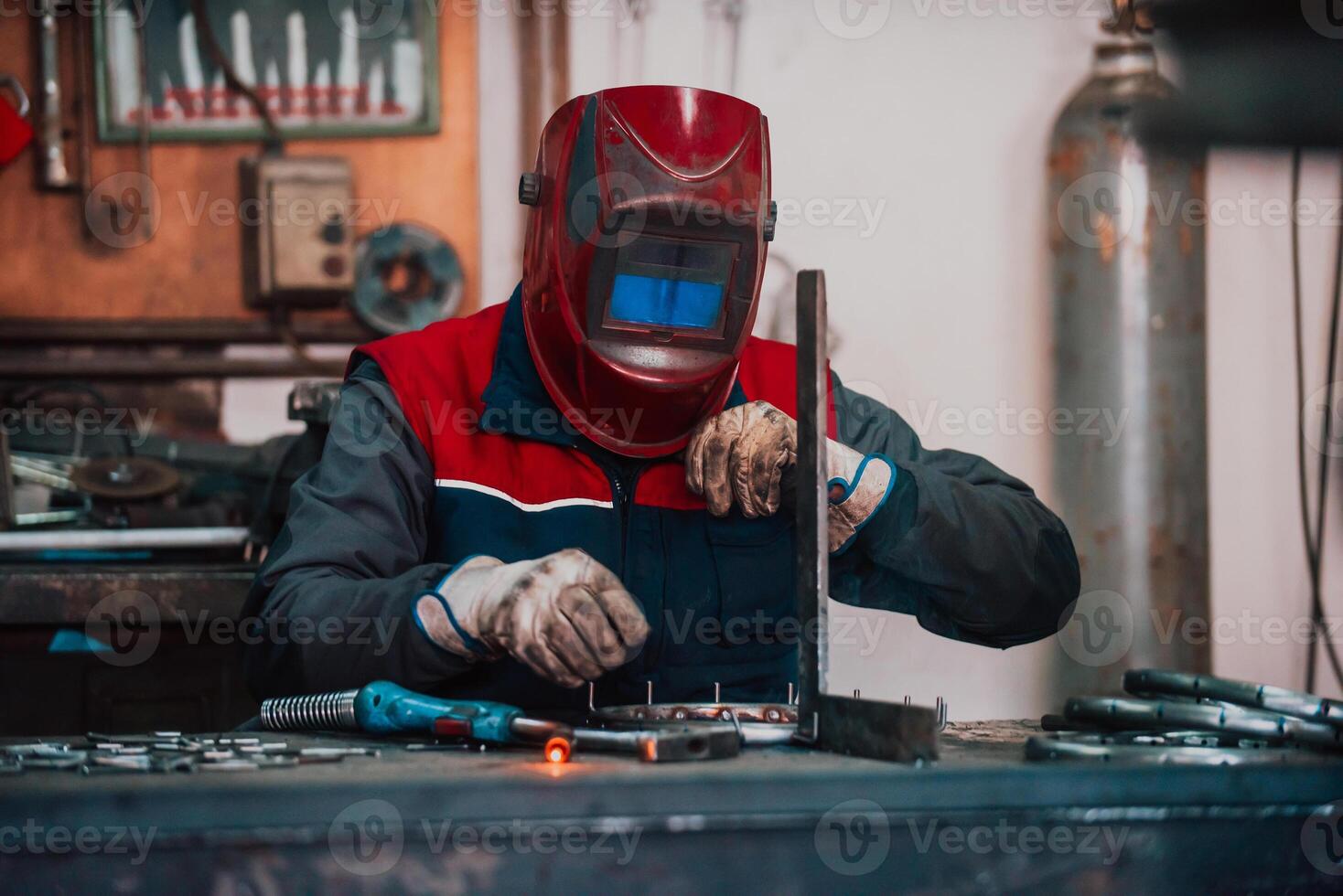 Close up welder in protective uniform and mask welding metal pipe on the industrial table with other workers behind in the industrial workshop. photo