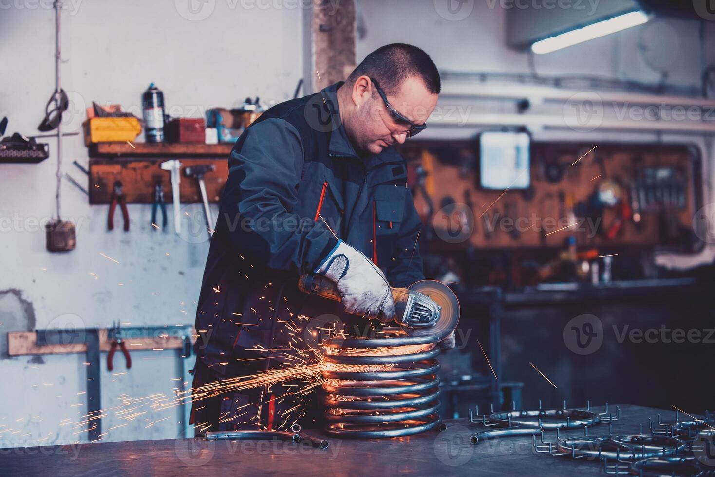 Locksmith in special clothes and goggles works in production. Metal processing with angle grinder. Sparks in metalworking. photo