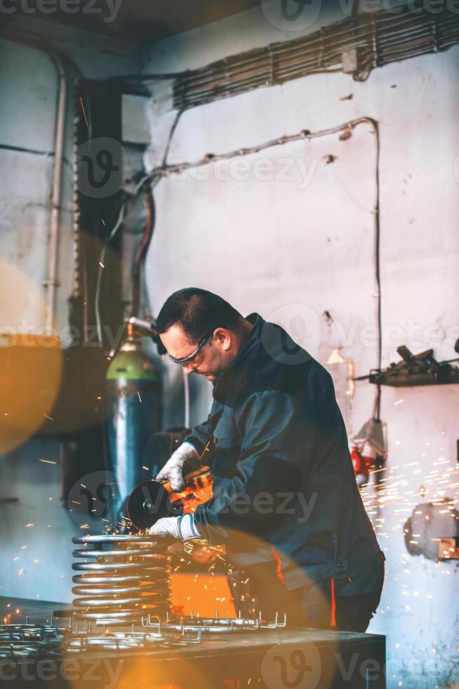 Locksmith in special clothes and goggles works in production. Metal processing with angle grinder. Sparks in metalworking. photo