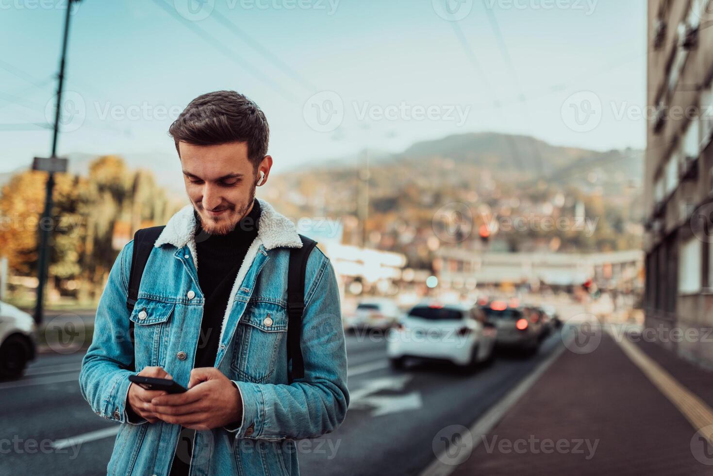 A student with a backpack using a smartphone on the street, checking email, writing messages and listening to music on headphones. photo